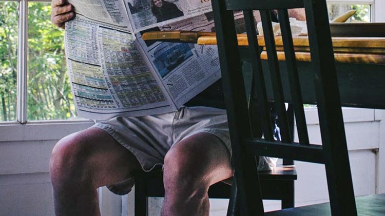 mann i shorts som sitter ved et bord og leser avisen. foto. 