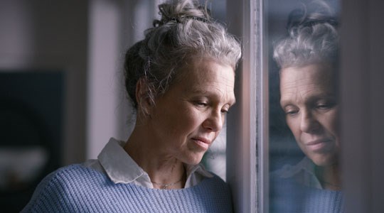 trist eldre kvinne med refleksjon av seg selv i vinduet. 