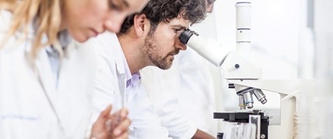 mann og dame i laboratoriefrakker ser i et mikroskop. foto. 