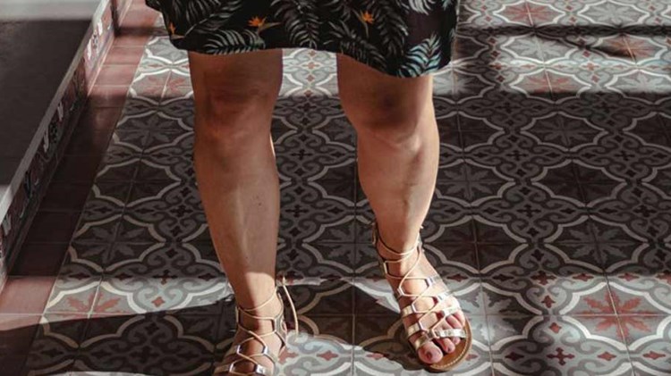 kvinne med bare legger går på flislagt gulv. Foto.
