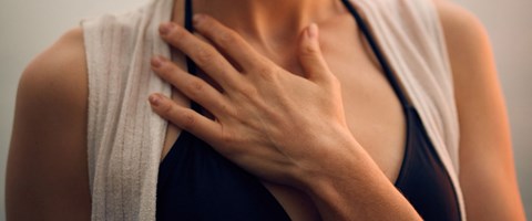 kvinne som holder seg til brystet med den ene hånden. foto. 