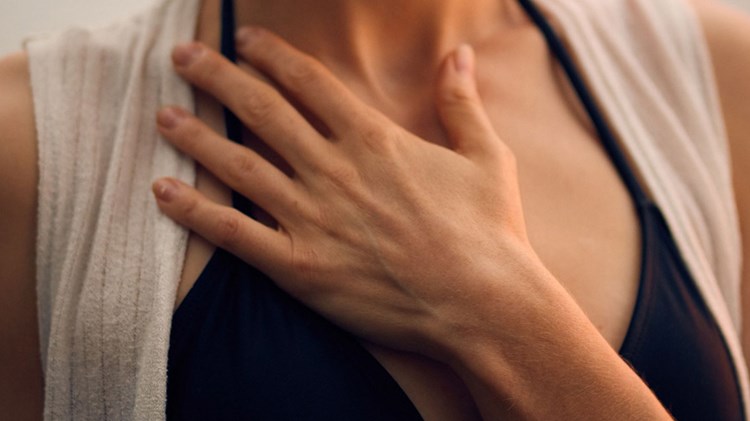 kvinne som holder seg til brystet med den ene hånden. foto. 