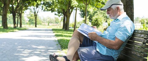 eldre mann iført støttestrømper leser avis på en benk. foto. 