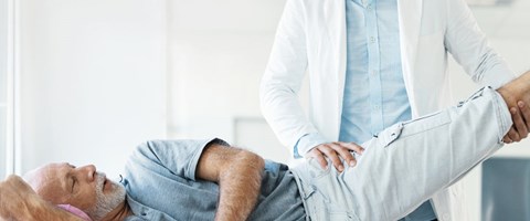 lege løfter på benet til en eldre mann som ligger på en undersøkelsesbenk. foto. 