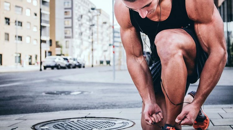 muskuløs og solbrun mann i treningstøy knyter på seg sko. foto. 