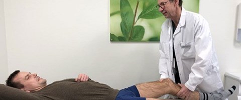 Dr. Aune sjekker benet til en pasient som ligger.