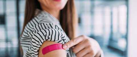 kvinne som peker på et rosa plaster på overarmen etter å ha tatt vaksine. 