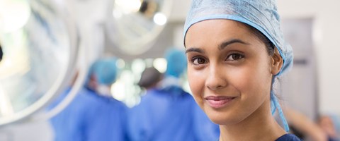 kvinnelig operasjonssykepleier med operasjonsteam i bakgrunnen. 